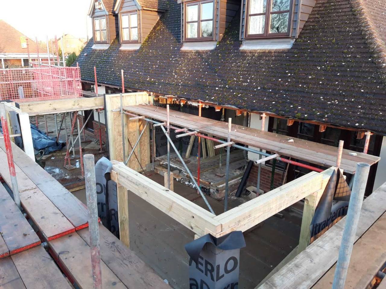 Timber frame of a single-storey rear extension under construction below a tiled roof with dormer windows