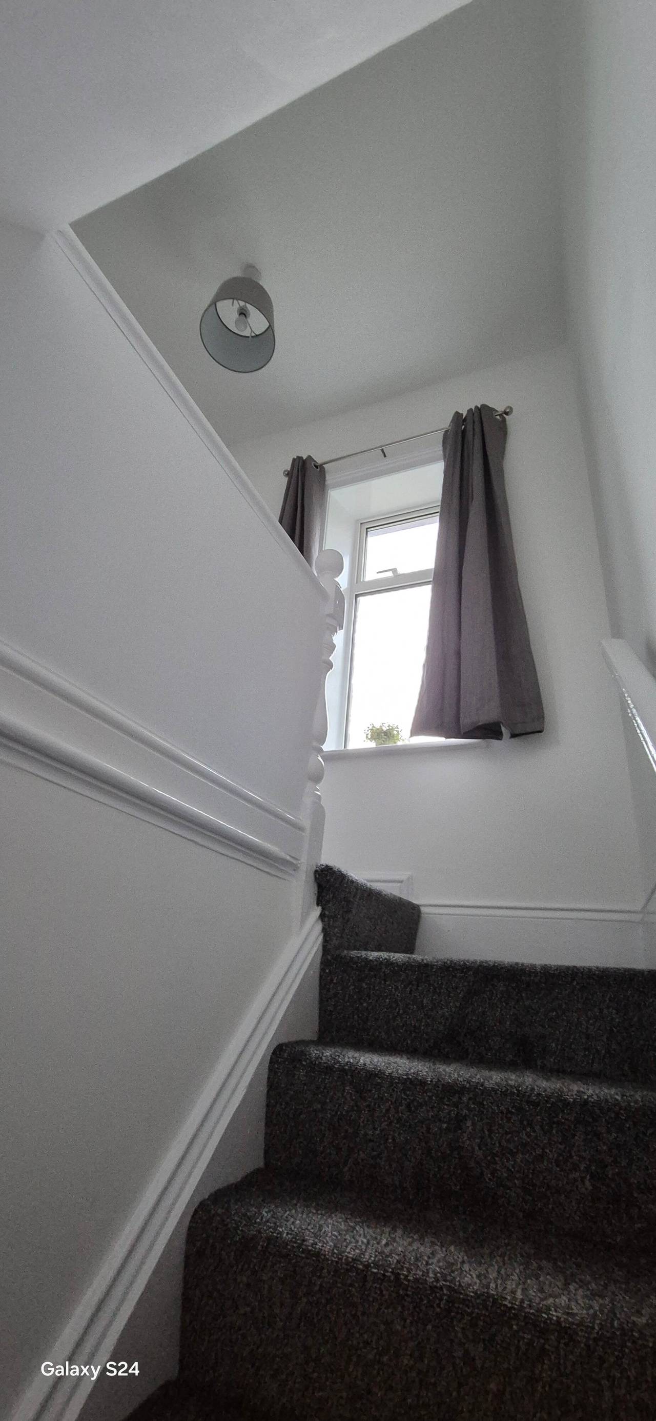 Freshly decorated white stairwell with new charcoal stair carpet, a dado rail and grey curtains at the landing window