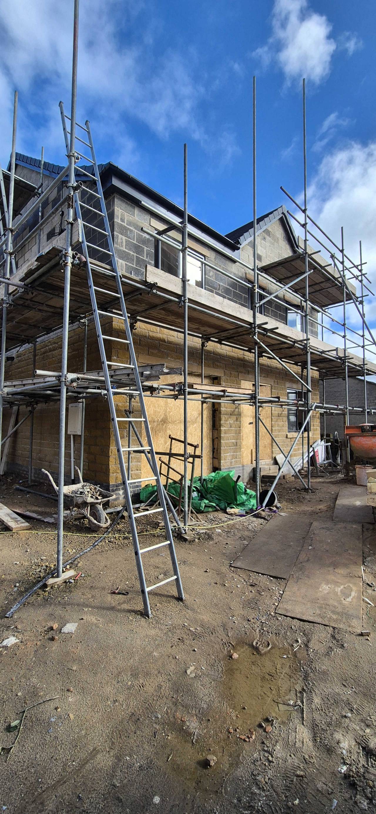 Two-storey new-build house in blockwork, wrapped in scaffolding under a bright blue sky