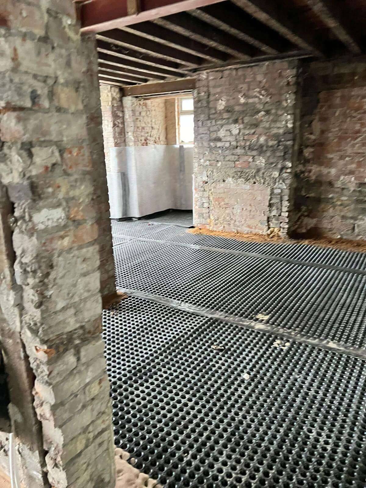 Room stripped back to bare brick with a studded drainage membrane laid across the floor during damp-proofing works