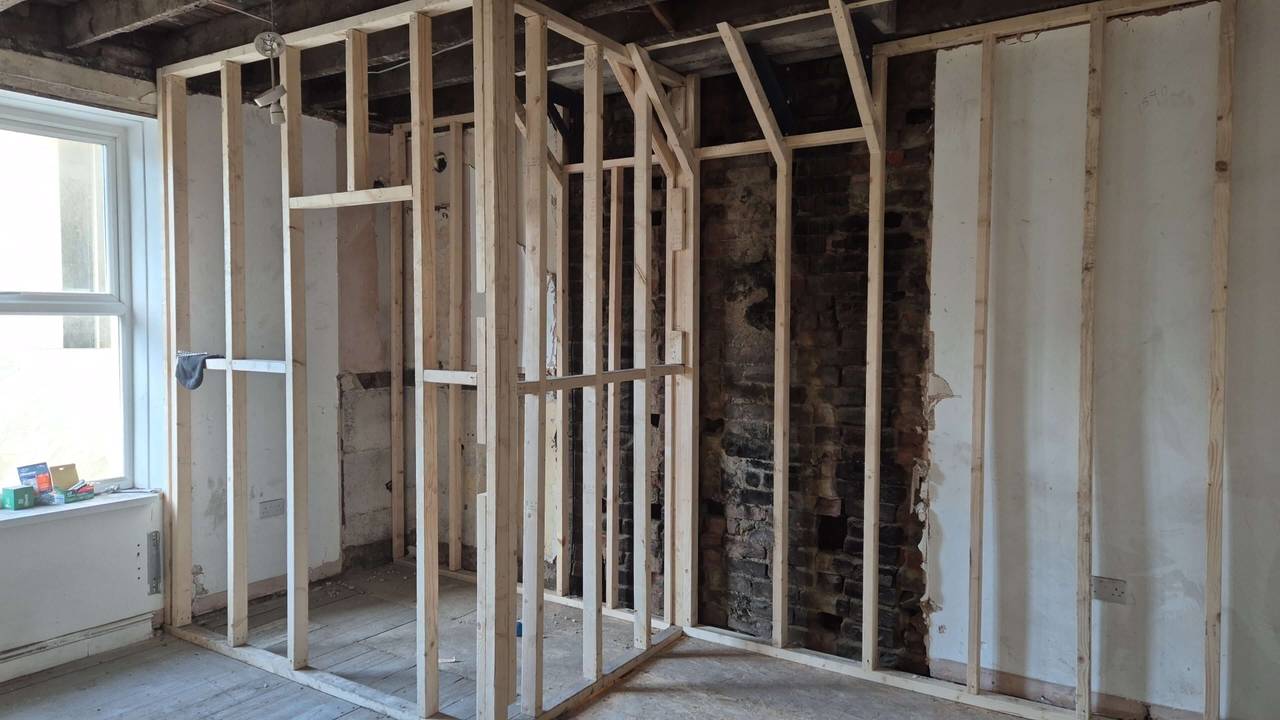 New timber stud walls framing out rooms inside a stripped-back room, in front of an exposed brick chimney breast