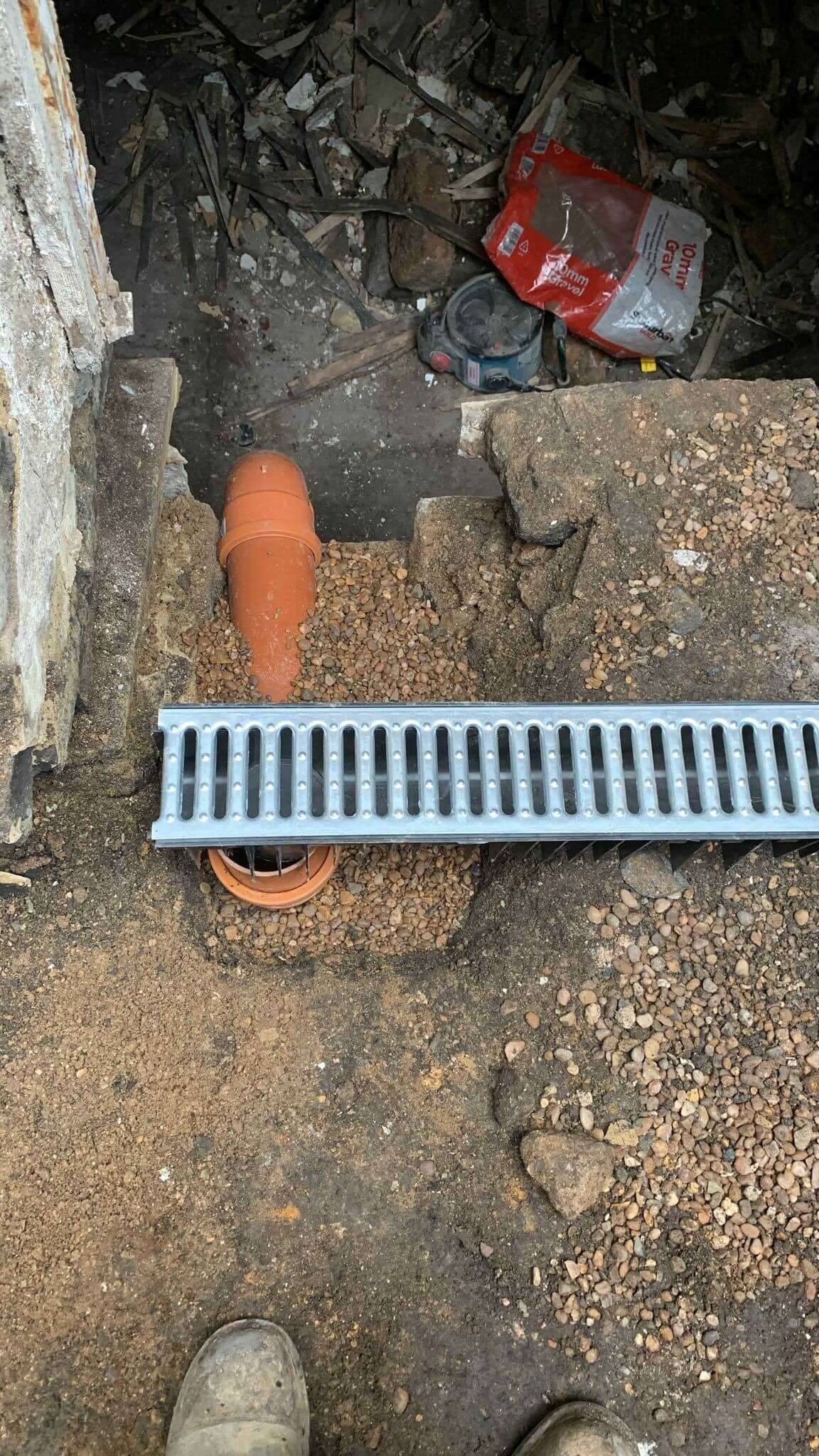 New drainage channel and orange underground pipework bedded in pea gravel during groundworks