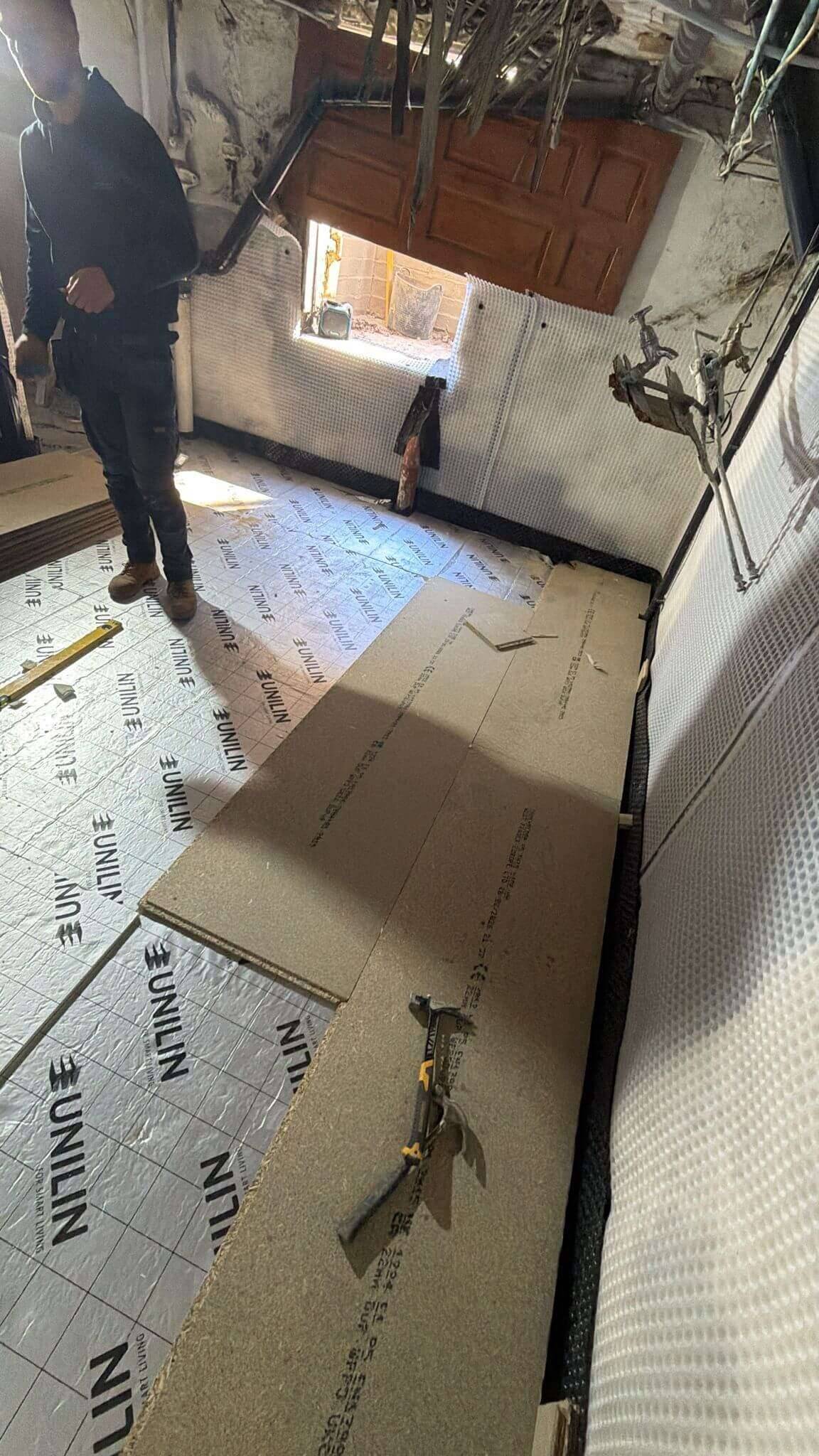 Basement floor being built up with foil-faced insulation boards and chipboard sheets inside a membrane-lined room